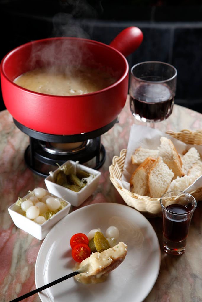 Warm cheese fondue served with bread, pickles, and wines, perfect for cozy gatherings.