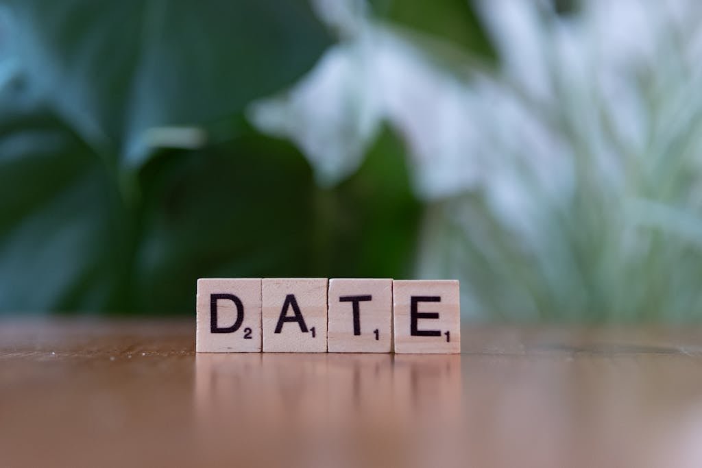 Wooden Scrabble tiles forming the word 'DATE' against a green blurred background.