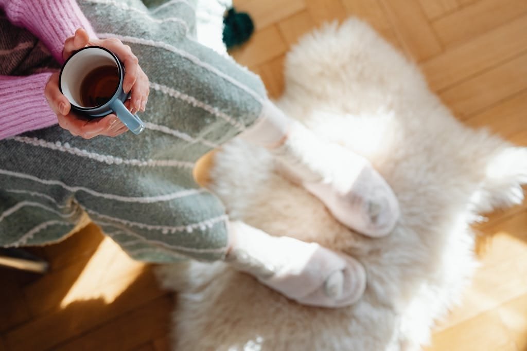 Person in cozy socks holding a warm drink on a fluffy rug, enjoying a peaceful morning.