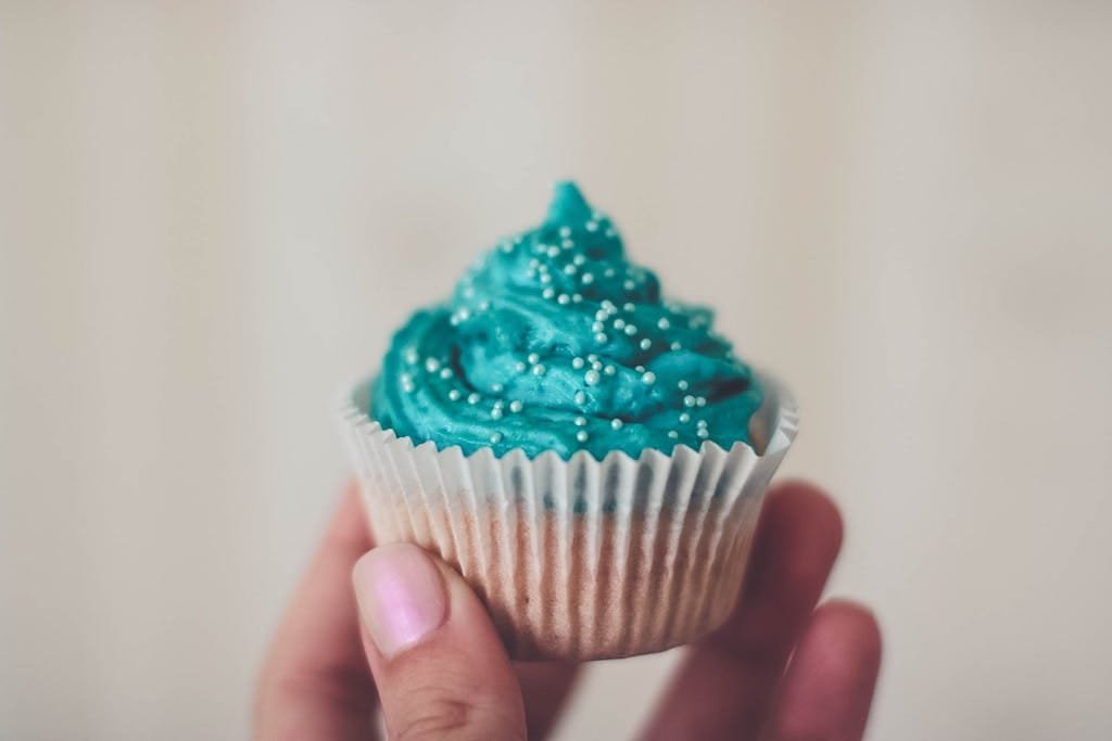 A hand-held cupcake with blue icing and sprinkles, perfect for dessert themes.