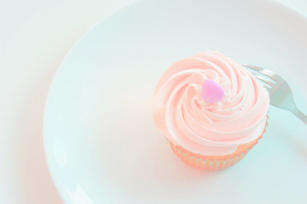 Aesthetic pastel cupcake with heart-shaped decoration on white plate.