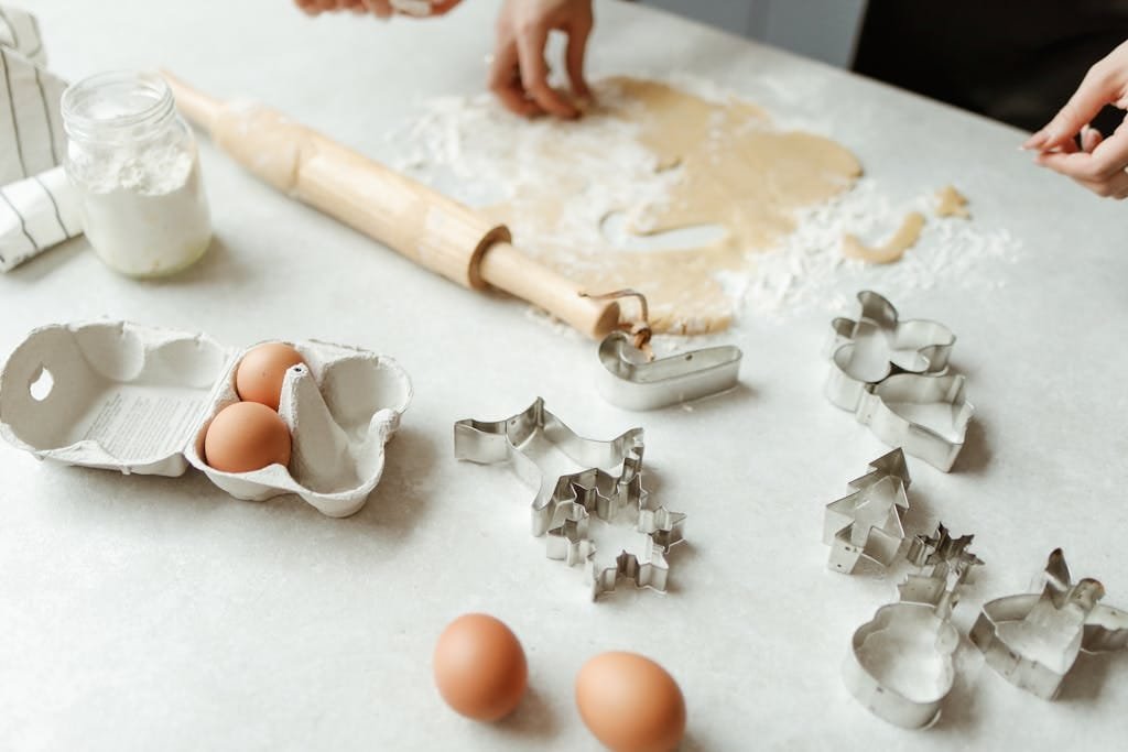 Preparing homemade cookies with dough, rolling pin, and cutters on kitchen counter.