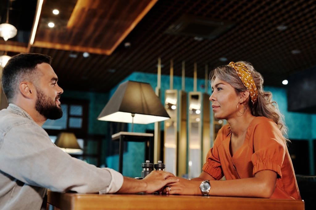 A couple holds hands and chats in a cozy café setting, creating a romantic atmosphere.