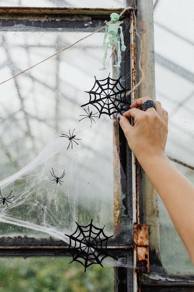 A hand decorates a window with Halloween spider web decor, creating a spooky ambiance.
