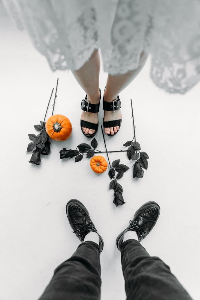 Top-down view of two people with black roses and pumpkins, a creative Halloween concept.
